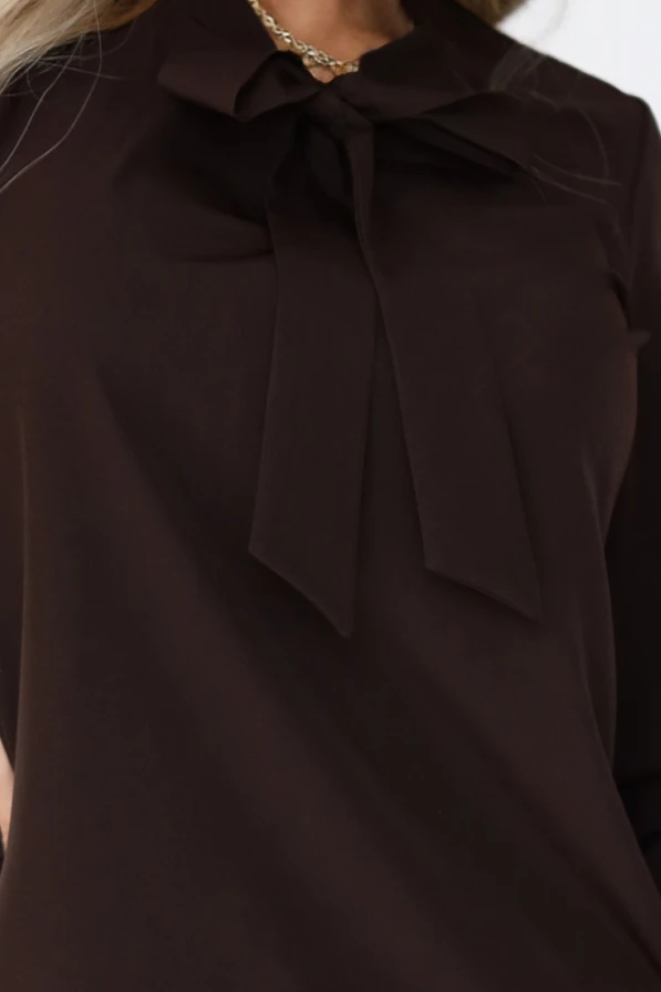 Modelka prezentuje elegancką bluzkę w kolorze czekoladowym z szerokimi mankietami i ozdobnym wiązaniem, styl biznesowy.