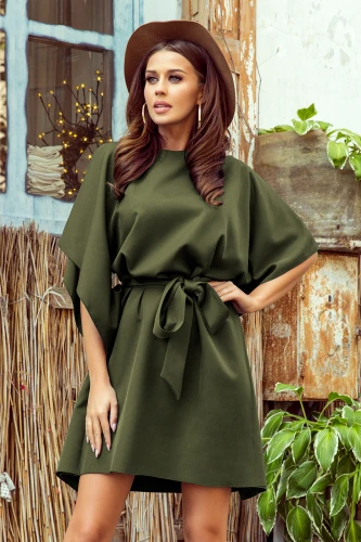 Elegantní zelené šaty s motýlími rukávy a páskem v pase dodávají sofistikovaný vzhled. Model je doplněn kloboukem a výraznými náušnicemi, což vytváří stylový a moderní outfit.}