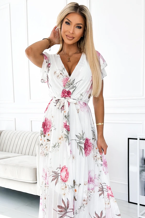 Na obrázku je elegantní plisované šaty s květinovým vzorem v jemných růžových a zelených tónech. Šaty mají krátké rukávy a zavazování v pase, což dodává ženský a sofistikovaný vzhled.