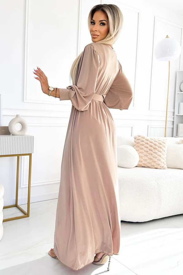 Dlouhé šaty v jemném béžovém odstínu s elegantním páskem v pase a volnými rukávy. Materiál působí lehce a splývavě, ideální pro formální příležitosti.
