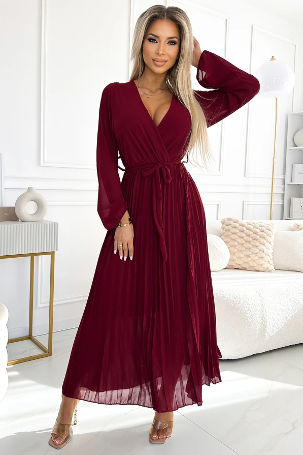 Dlouhé plisované šaty z šifonu v sytě vínové barvě s elegantním zavazováním v pase. Šaty mají hluboký výstřih a dlouhé rukávy, ideální pro slavnostní příležitosti.