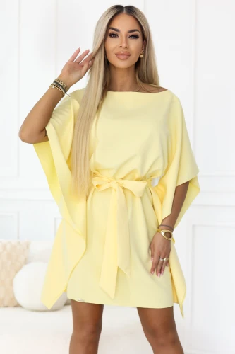 Modelka představuje pastelové citronové mini šaty Numoco s volnými rukávy ve stylu kimona a vázáním v pase, které krásně zvýrazňuje postavu. Elegantní, lehká kreace ideální na léto, večírky a stylové vycházky.}