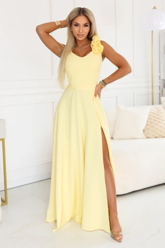 Elegantní žluté maxi šaty Numoco Polsko s květinovou ozdobou na rameni, výstřihem do V, vysokým rozparkem, zvýrazněným pasem a vzdušnou sukní, ideální na svatbu, maturitní ples, ples a letní slavnosti.}