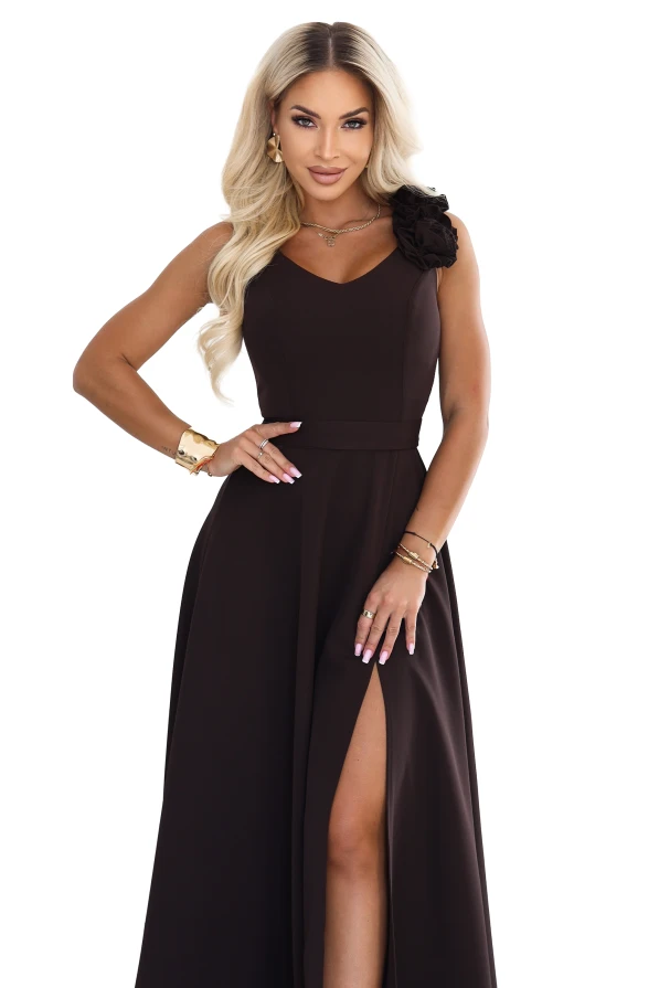 Modelka v elegantních, čokoládově hnědých maxi šatech s výstřihem do srdíčka, rozparkem na noze a ozdobným květem na rameni.