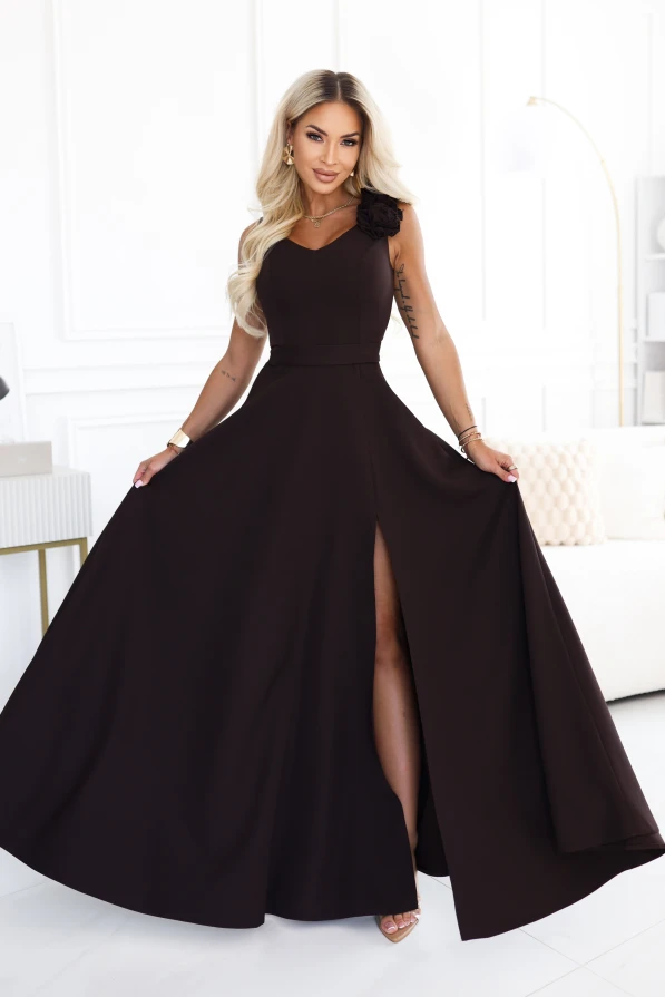Modelka v elegantních, čokoládově hnědých maxi šatech s výstřihem do srdíčka, rozparkem na noze a ozdobným květem na rameni.