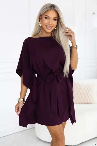 Modelka v šatech kimono Numoco v barvě zralé švestky s výstřihem do lodičky, širokými rukávy, páskem vázaným v pase a řasenými boky, v délce těsně nad kolena.}