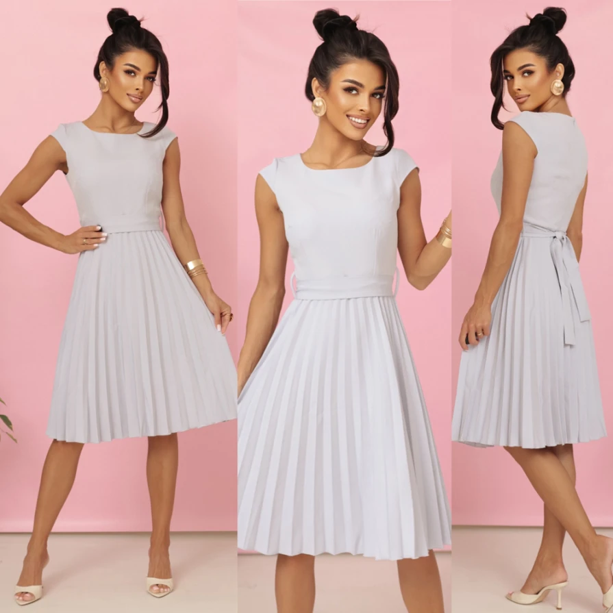 Modelka w eleganckiej plisowanej sukience midi marki Numoco w kolorze jasnoszarym, z krótkim rękawkiem i wiązaniem w talii, prezentująca kreację idealną na wesele, komunię i inne uroczystości.