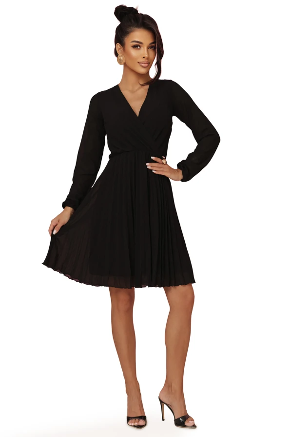 Modelka prezentuje elegancką czarną szyfonową sukienkę marki Numoco z długim rękawem, kopertowym dekoltem i plisowanym dołem – idealną na wieczór, wesele lub specjalne okazje. Produkt polski, sfotografowany na różowym tle.