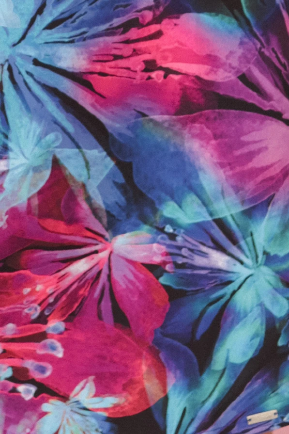 Modelka prezentuje kolorową sukienkę oversize Numoco z tropikalnym wzorem i rękawami 3/4 z wiązaniem – idealna propozycja na lato, produkt polski.