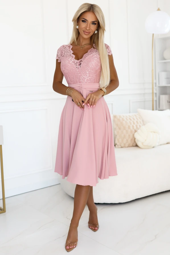 Modelka prezentuje elegancką sukienkę z koronkową górą i rozkloszowanym dołem w kolorze pudrowego różu; kobieca stylizacja idealna na wesele i wyjątkowe okazje, produkt polski marki Numoco.