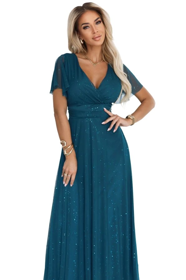 Modelka prezentuje elegancką długą sukienkę MELANIA w kolorze butelkowej zieleni z błyszczącym materiałem i dekoltem V.