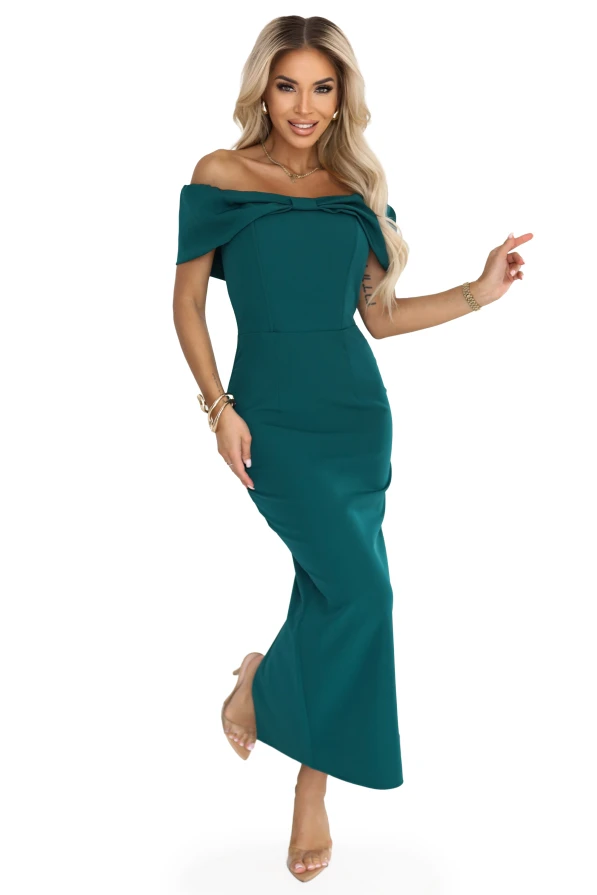 Wieczorowa sukienka maxi w odcieniu butelkowej zieleni z kokardą na dekolcie, pokazana na modelce w eleganckiej aranżacji.