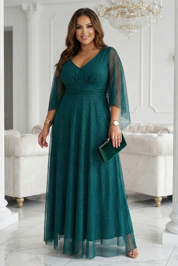 Modelka w szmaragdowej wieczorowej sukience plus size maxi z brokatowym połyskiem i rękawami typu motyl w jasnym wnętrzu.