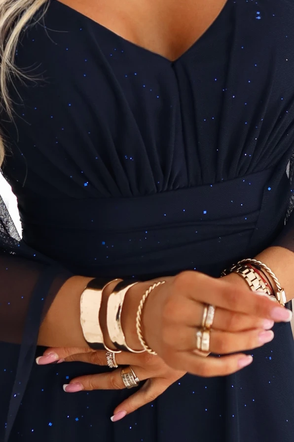 Granatowa brokatowa sukienka maxi z dekoltem V i rękawami motyl, idealna również dla kobiet plus size, prezentowana przez modelkę w jasnym wnętrzu.